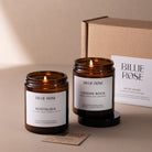 Two lit candles from Billie Rose with their packaging on a beige background