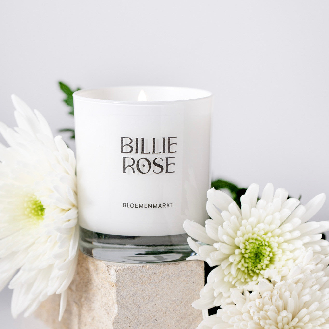 White candle with 'Billie Rose' branding surrounded by white flowers on a light background