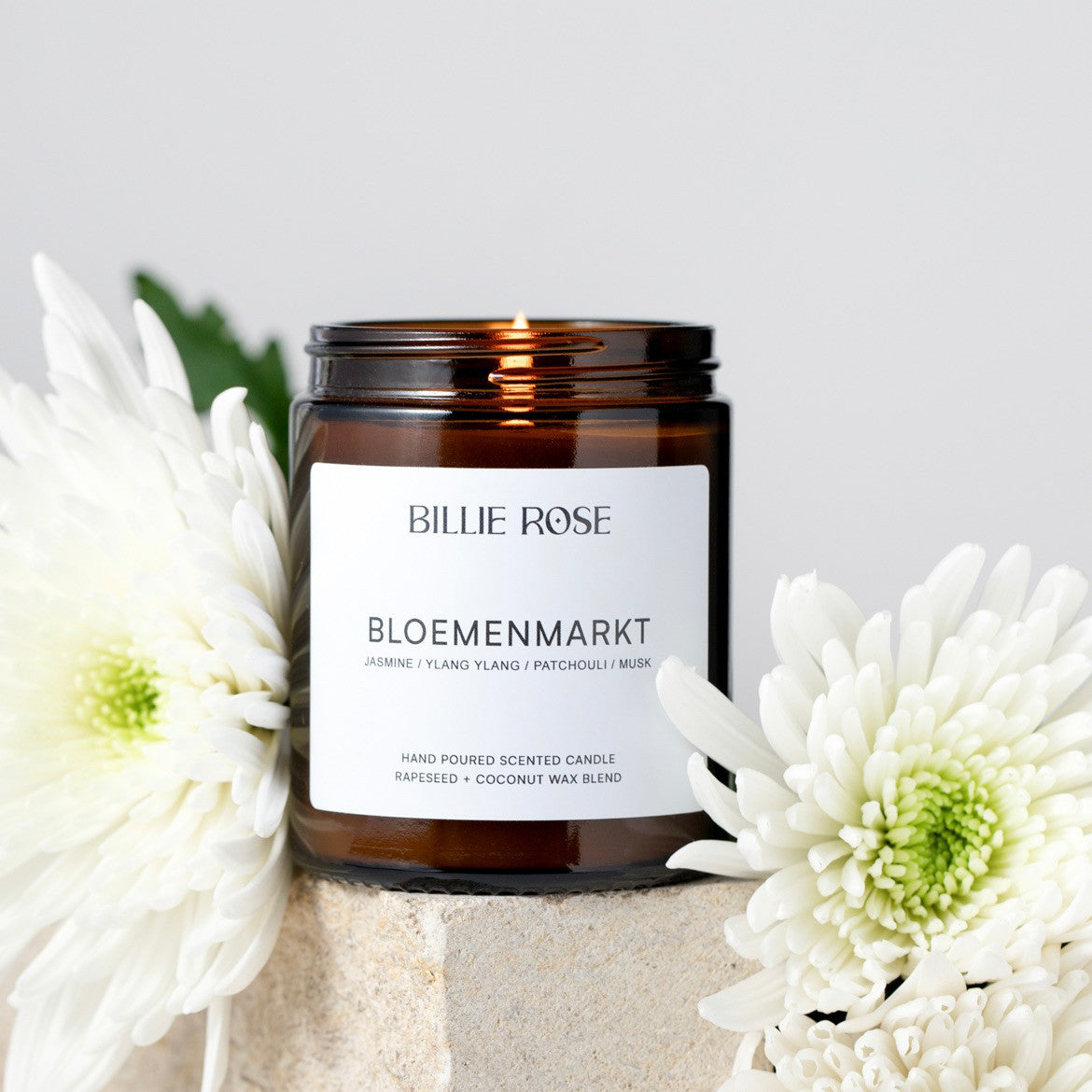 Brown candle jar with 'Billie Rose' label surrounded by white flowers on a light background