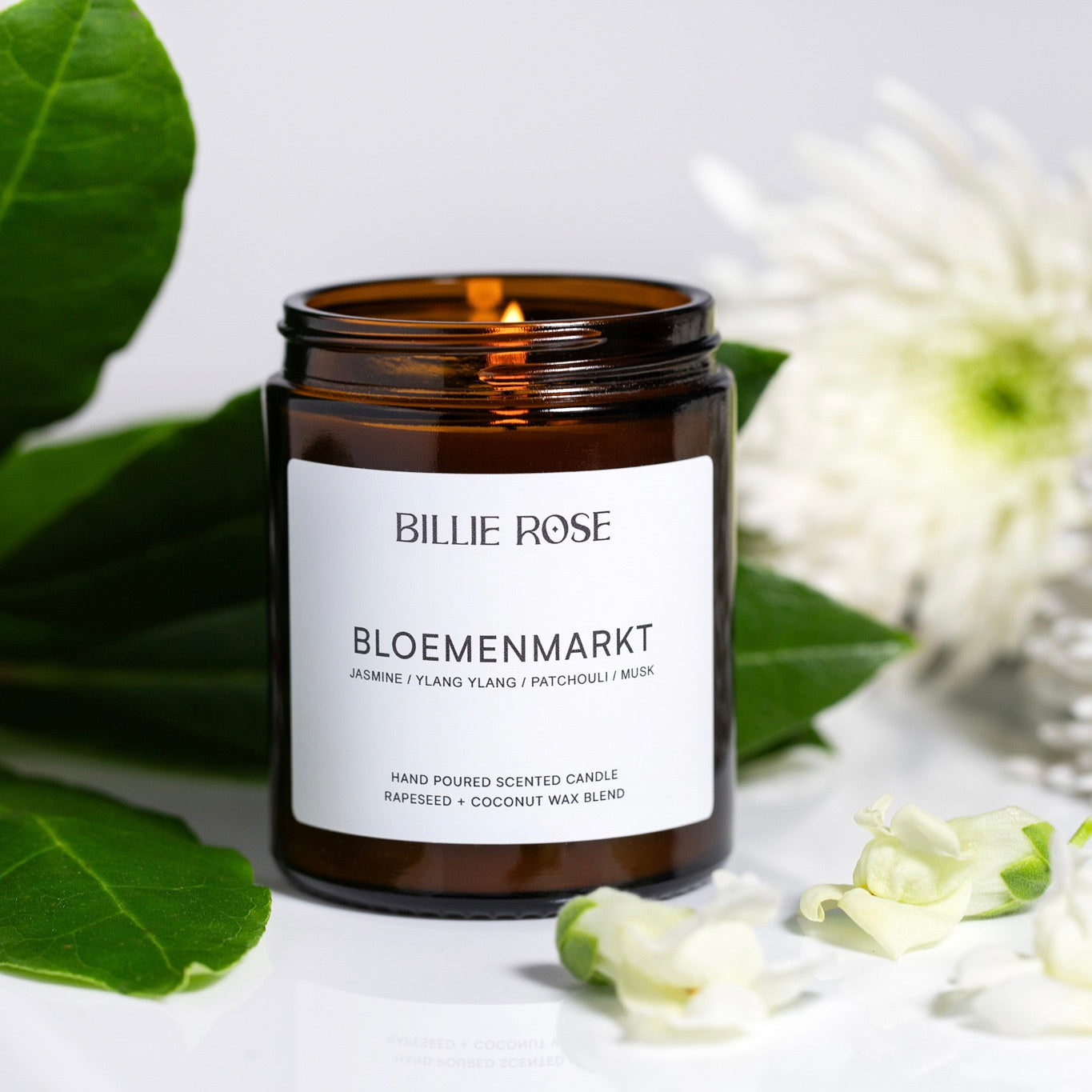 lit scented candle surrounded by green leaves and white flowers