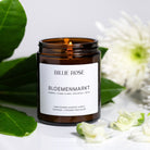 lit scented candle surrounded by green leaves and white flowers