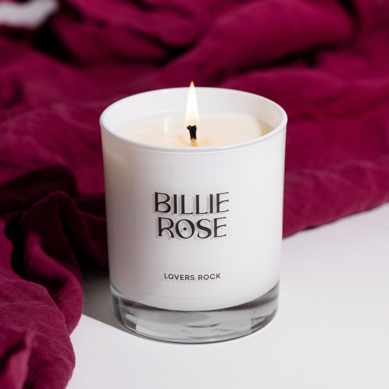 Candle in a white container with 'Billie Rose' branding on a red fabric background