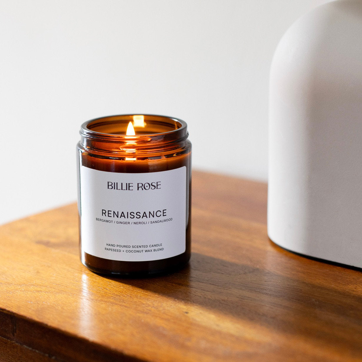 Billie Rose Renaissance candle in amber glass on a wooden surface with a white background