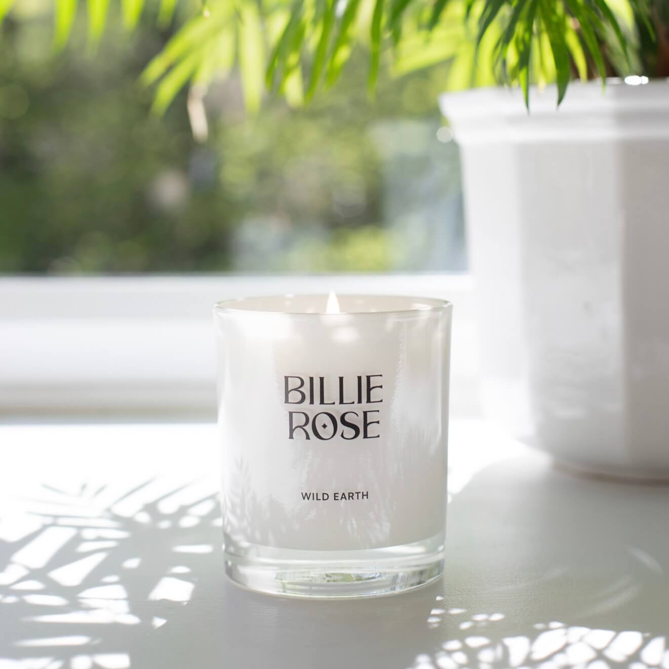 Billie Rose candle on a window ledge with greenery in the background