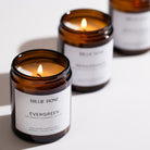 Three lit candles in amber jars with white labels on a light background