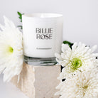 White candle with 'Billie Rose' branding surrounded by white flowers on a light background