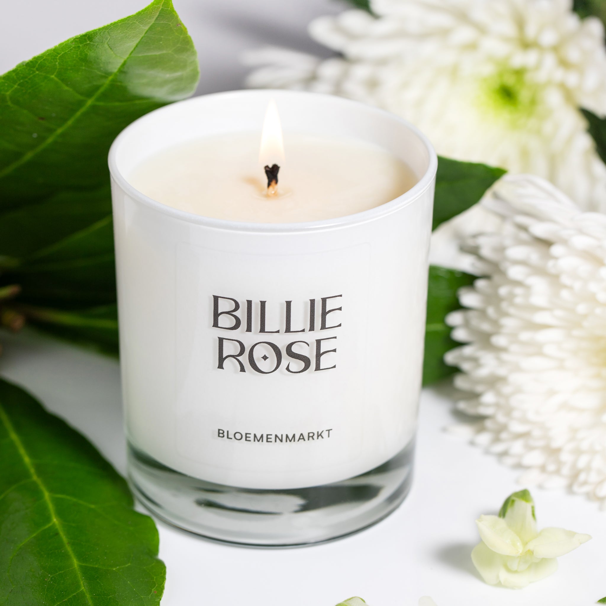 lit candle in white glass surrounded by flowers