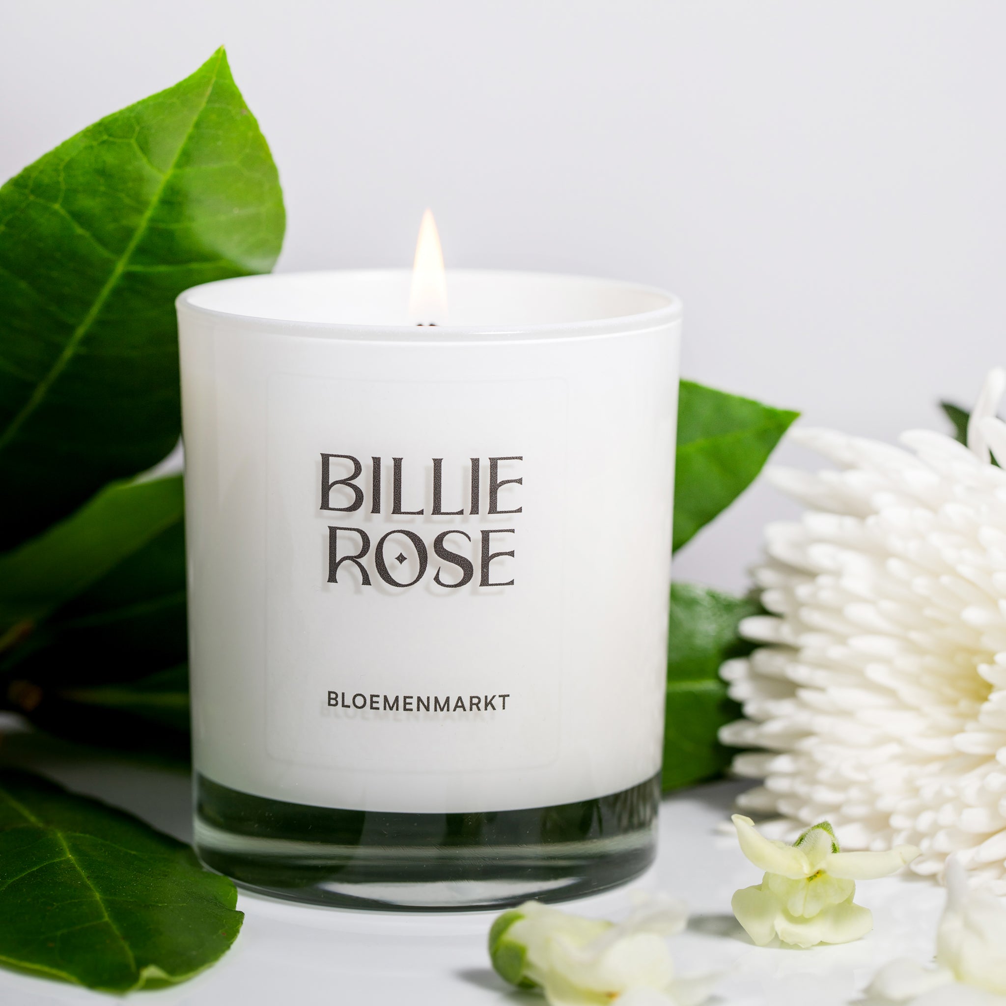lit candle in white glass surrounded by flowers
