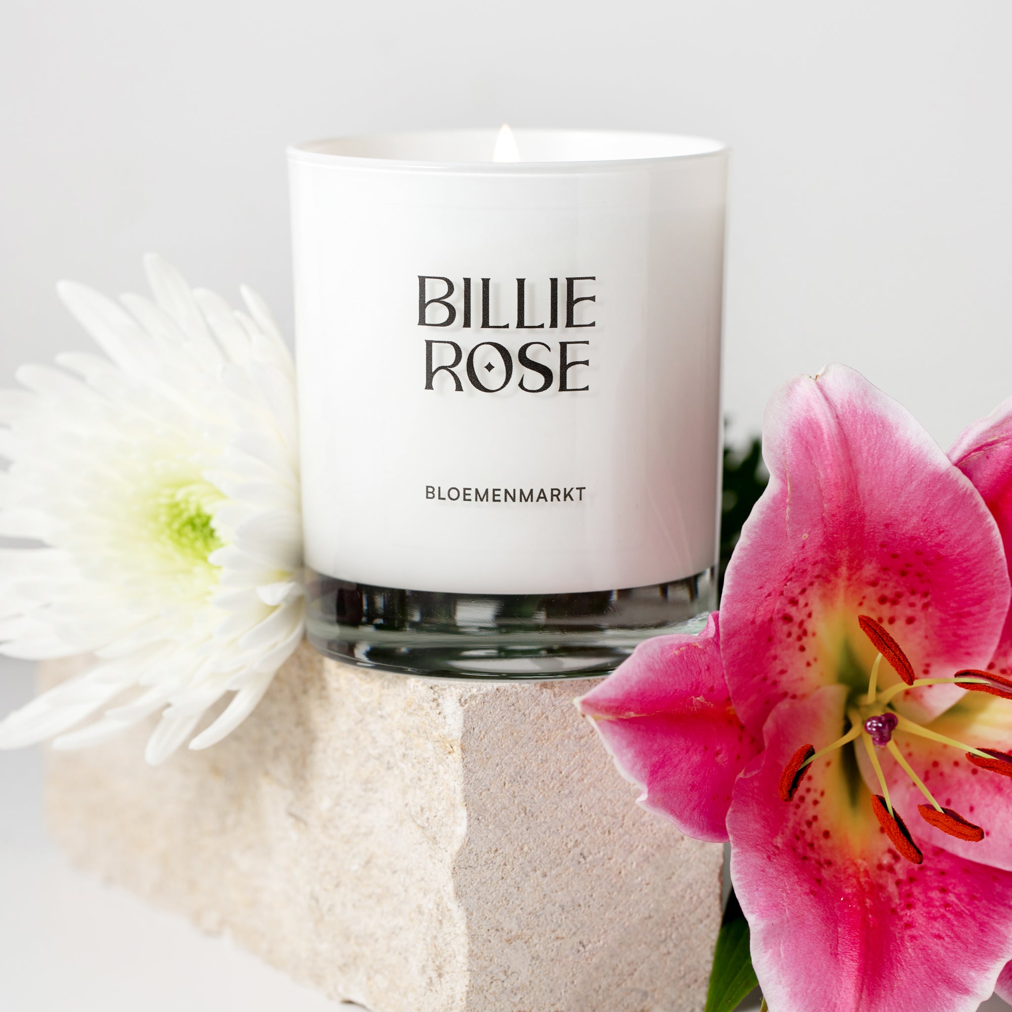 lit candle in white glass  on concrete block surrounded by flowers