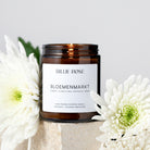 Brown candle jar with 'Billie Rose' label surrounded by white flowers on a light background