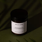 amber jar candle with lid on green background with tree shadows