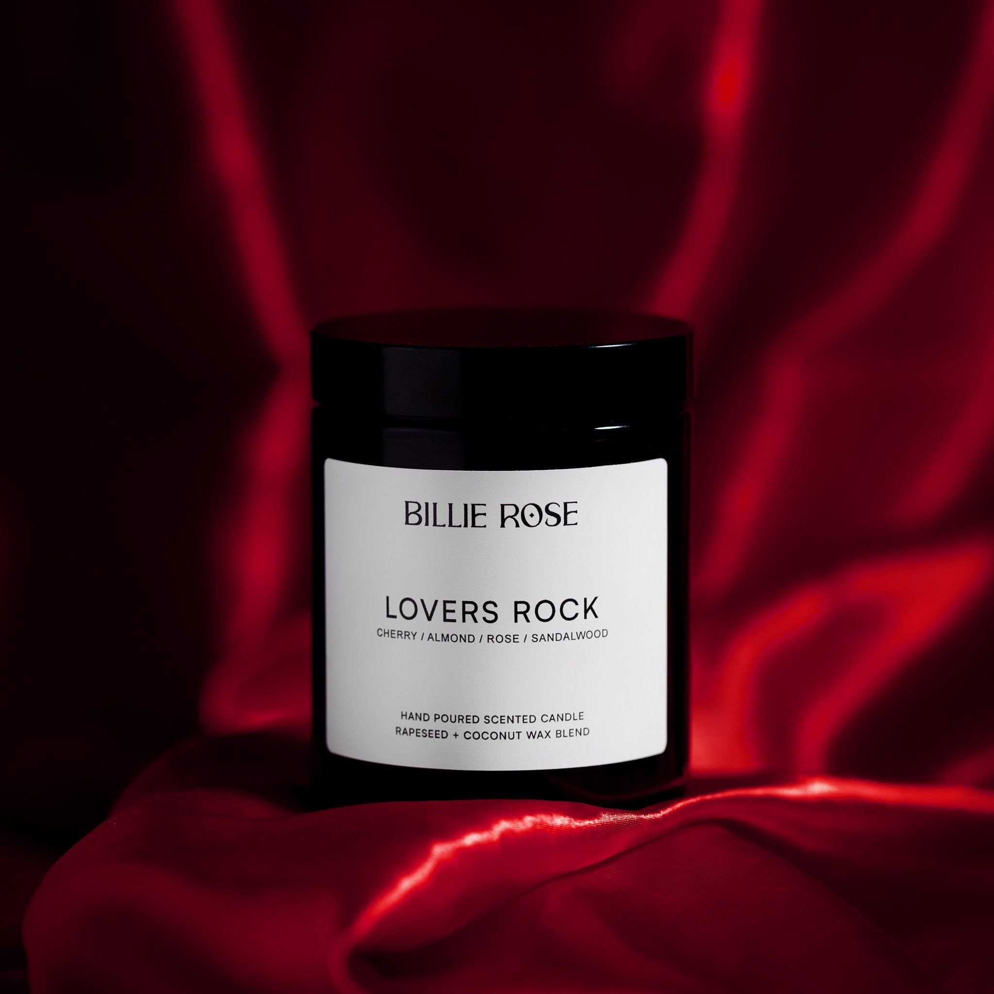Candle jar labeled 'Lovers Rock' by Billie Rose on a red fabric background