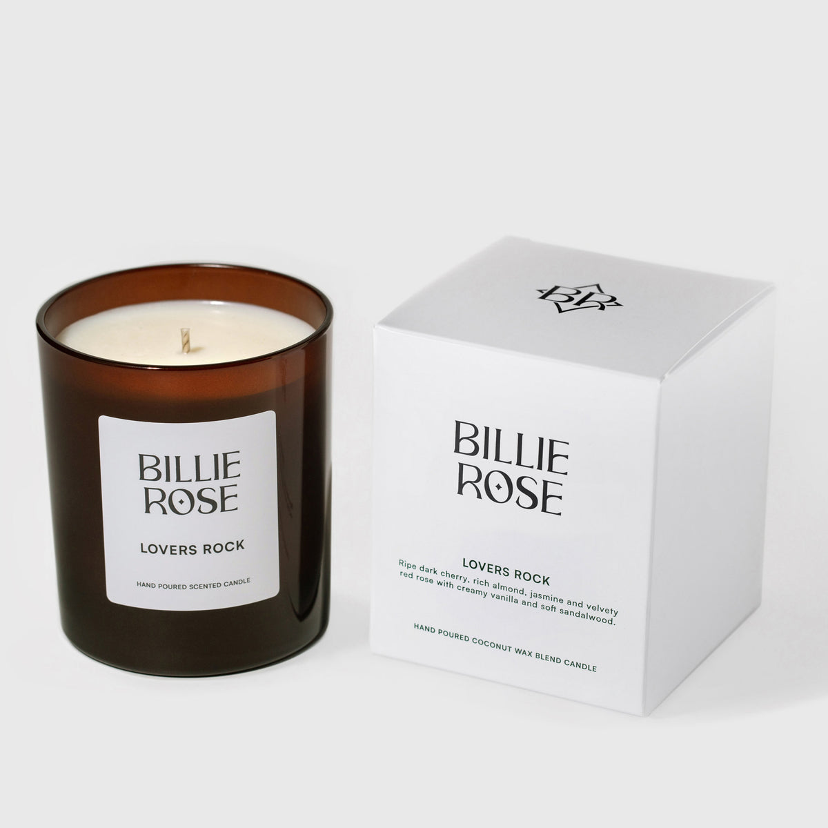 An amber glass jar candle with a white label reading BILLIE ROSE LOVERS ROCK, shown next to its white product box on a light grey background.