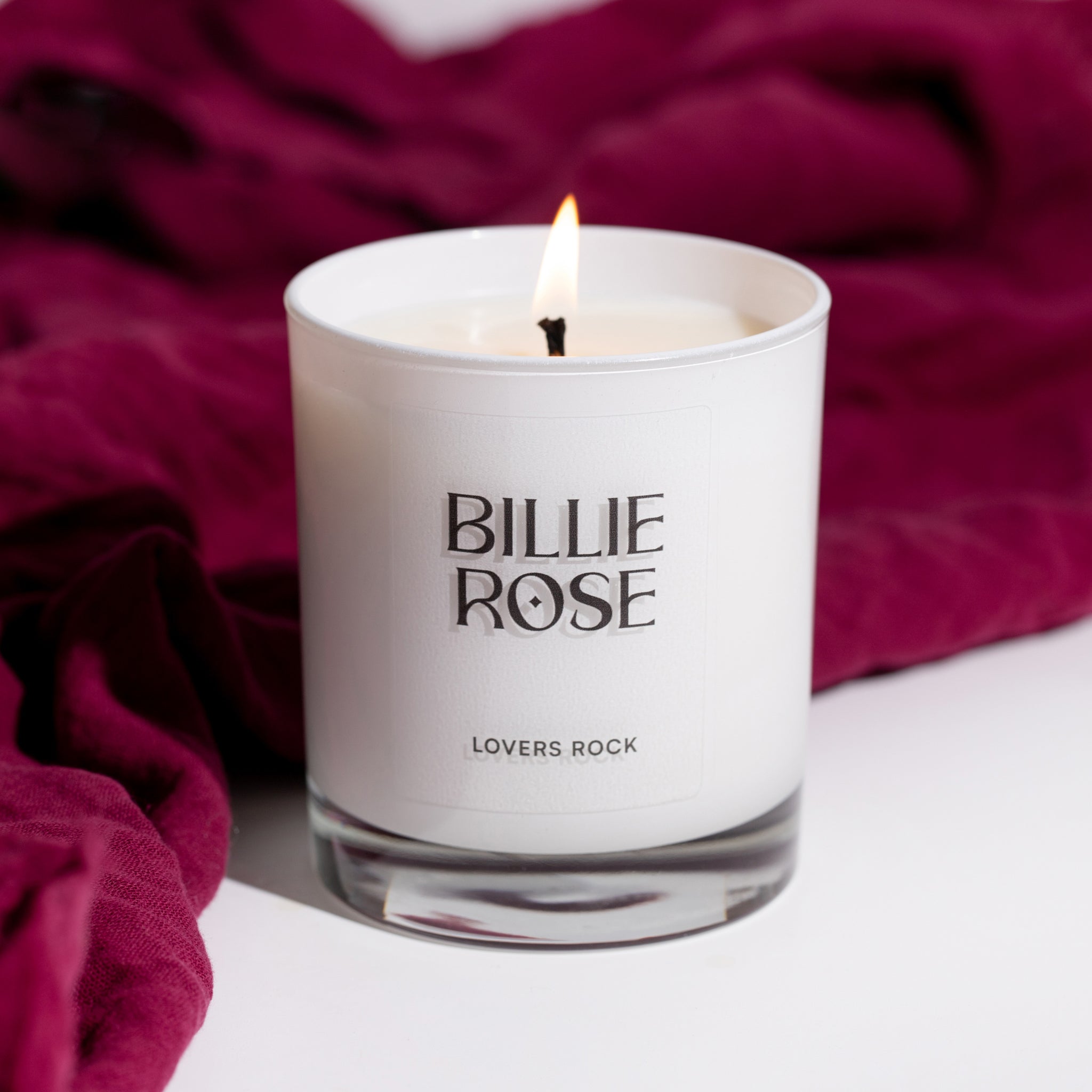 Billie Rose candle with a flame on a red fabric background