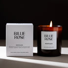 Billie Rose Nostalgia hand-poured rapeseed and coconut wax candle shown with its white product box and a lit amber glass jar candle on a dark surface against a black background.