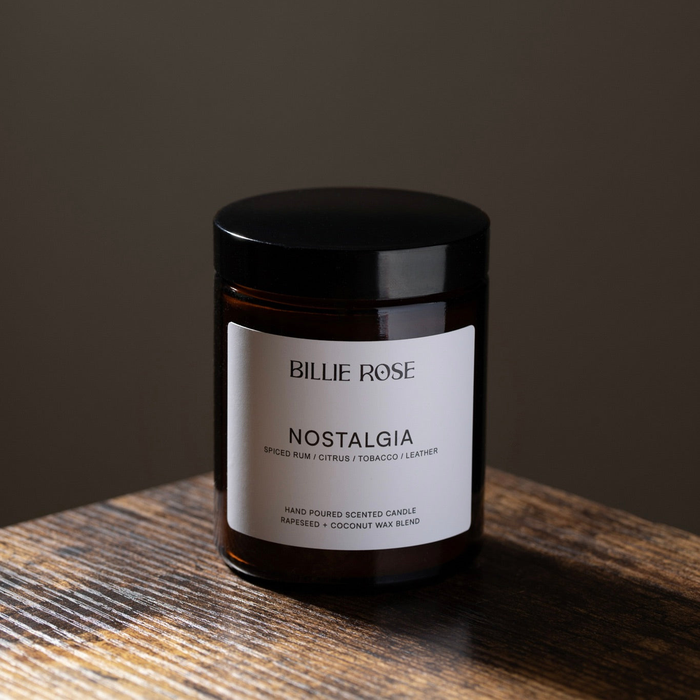 Candle jar labeled 'Nostalgia' by Billie Rose on a wooden surface with a dark background