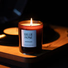 A lit Billie Rose Nostalgia scented candle in a dark amber glass jar, set on a wooden record player with a warm, dimly lit background.