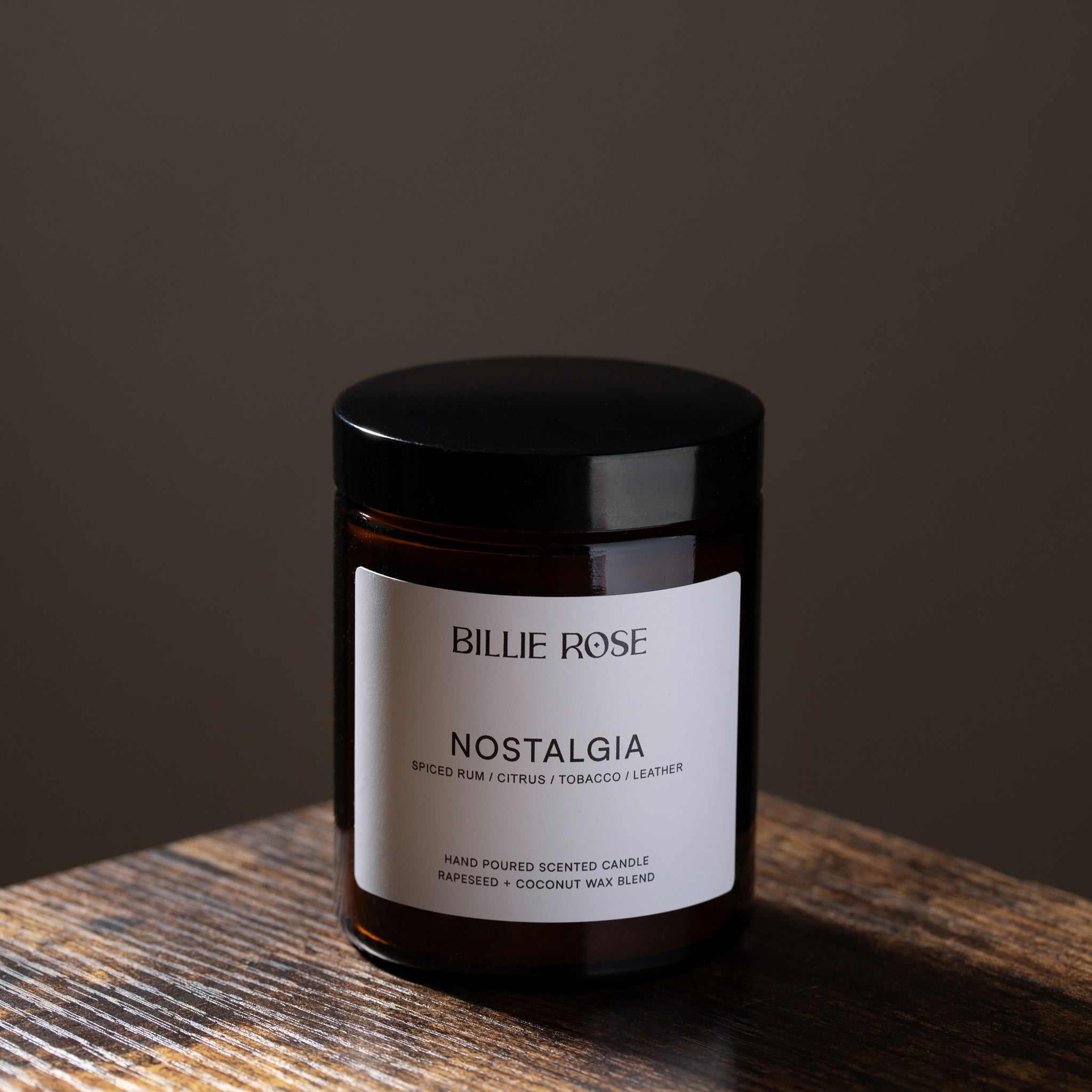 Candle jar labeled 'Nostalgia' by Billie Rose on a wooden surface with a dark background
