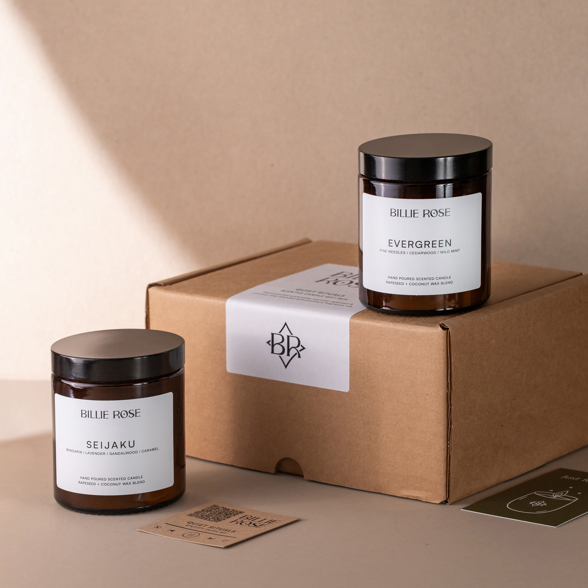 Two candles labelled 'Seijaku' and 'Evergreen' by Billie Rose on a Kraft cardboard box with a beige background.