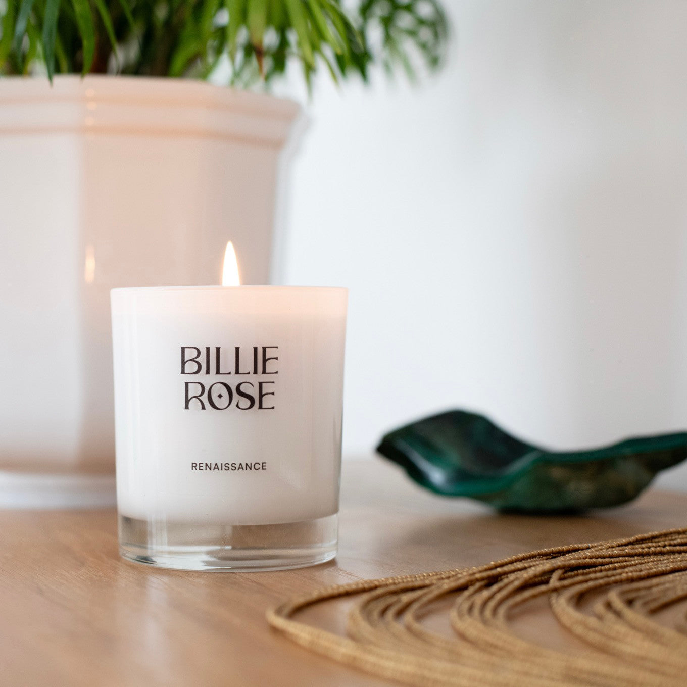 Billie Rose candle on a table with a plant and decorative object in the background