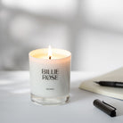 Lit candle with 'Billie Rose' branding on a light surface with a pen and notebook.