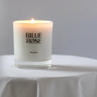 Candle with 'Billie Rose' branding on a white surface and gray background