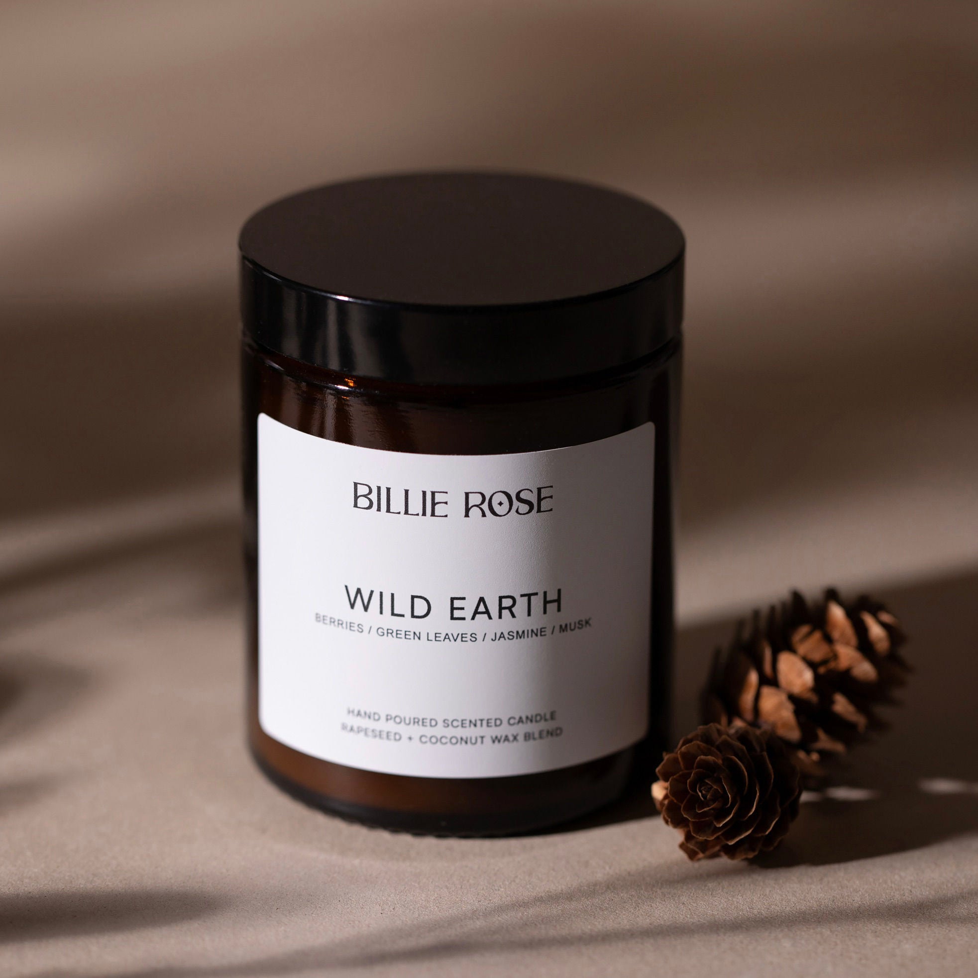 Candle jar labeled 'Billie Rose Wild Earth' with a pine cone on a beige background