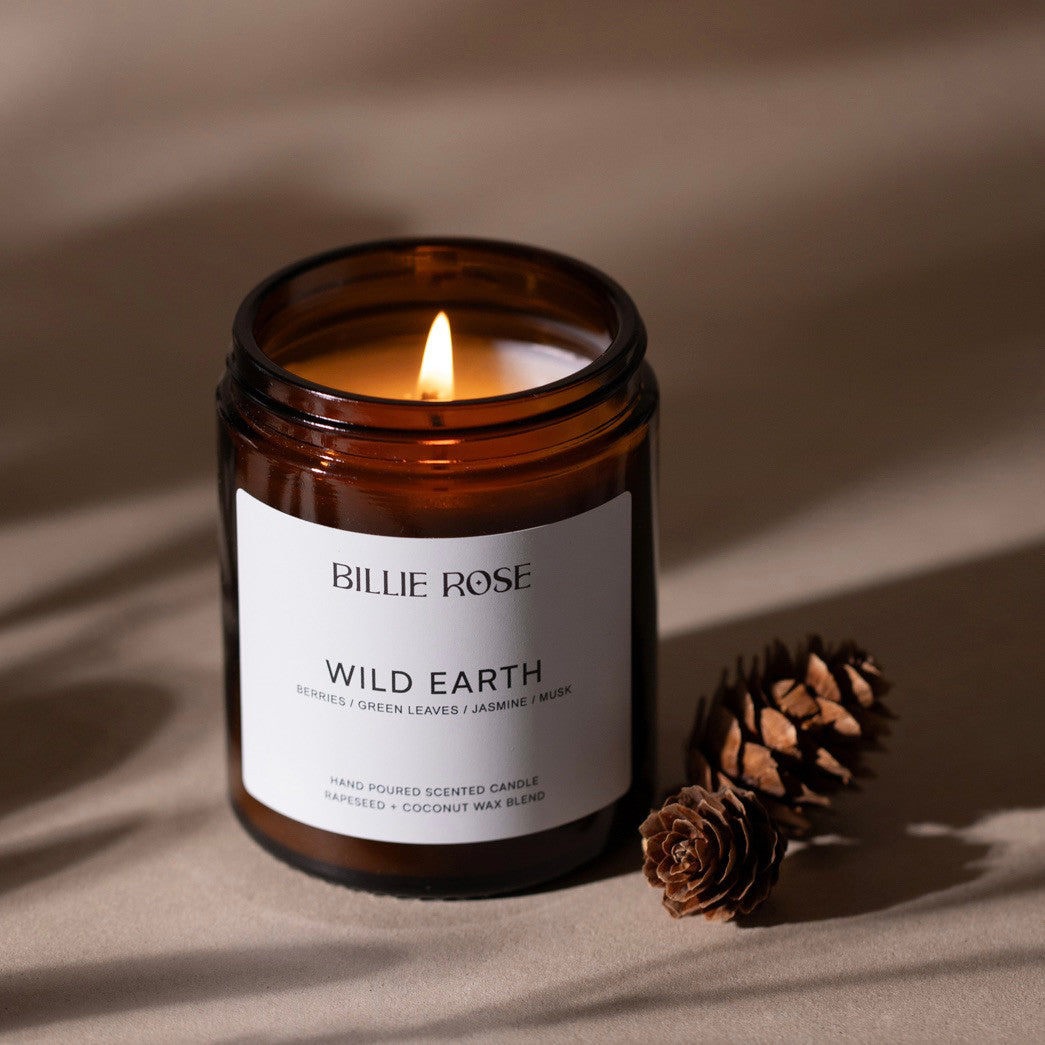 Billie Rose Wild Earth candle in a brown jar with a lit candle on a beige background