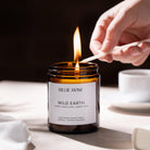 Candle labelled 'Billie Rose Wild Earth' being lit with a match on a neutral background.