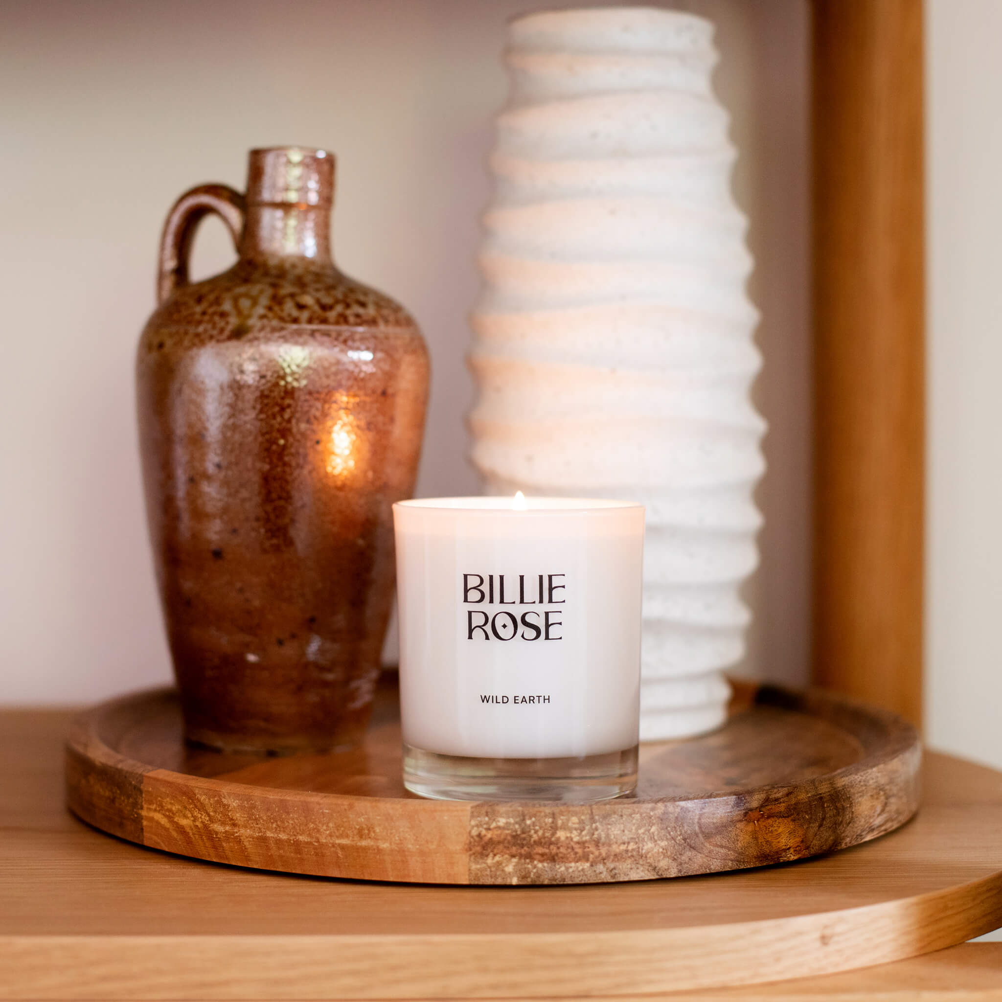 Candle labelled 'Billie Rose' on a wooden surface with decorative items.