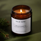 lit scented Wild Earth candle on green background with leaves