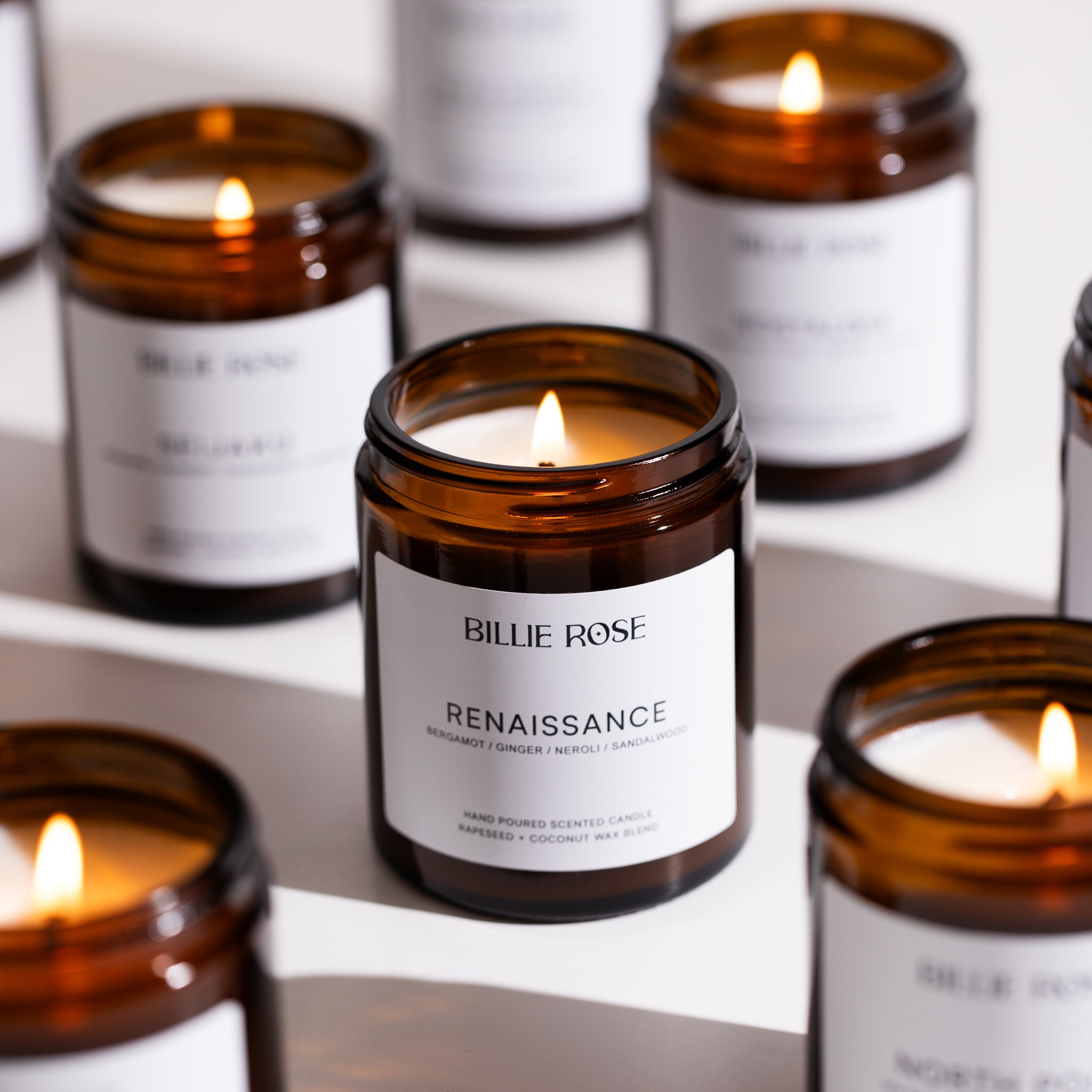 Lit candles in amber glass jars with white labels on a white surface