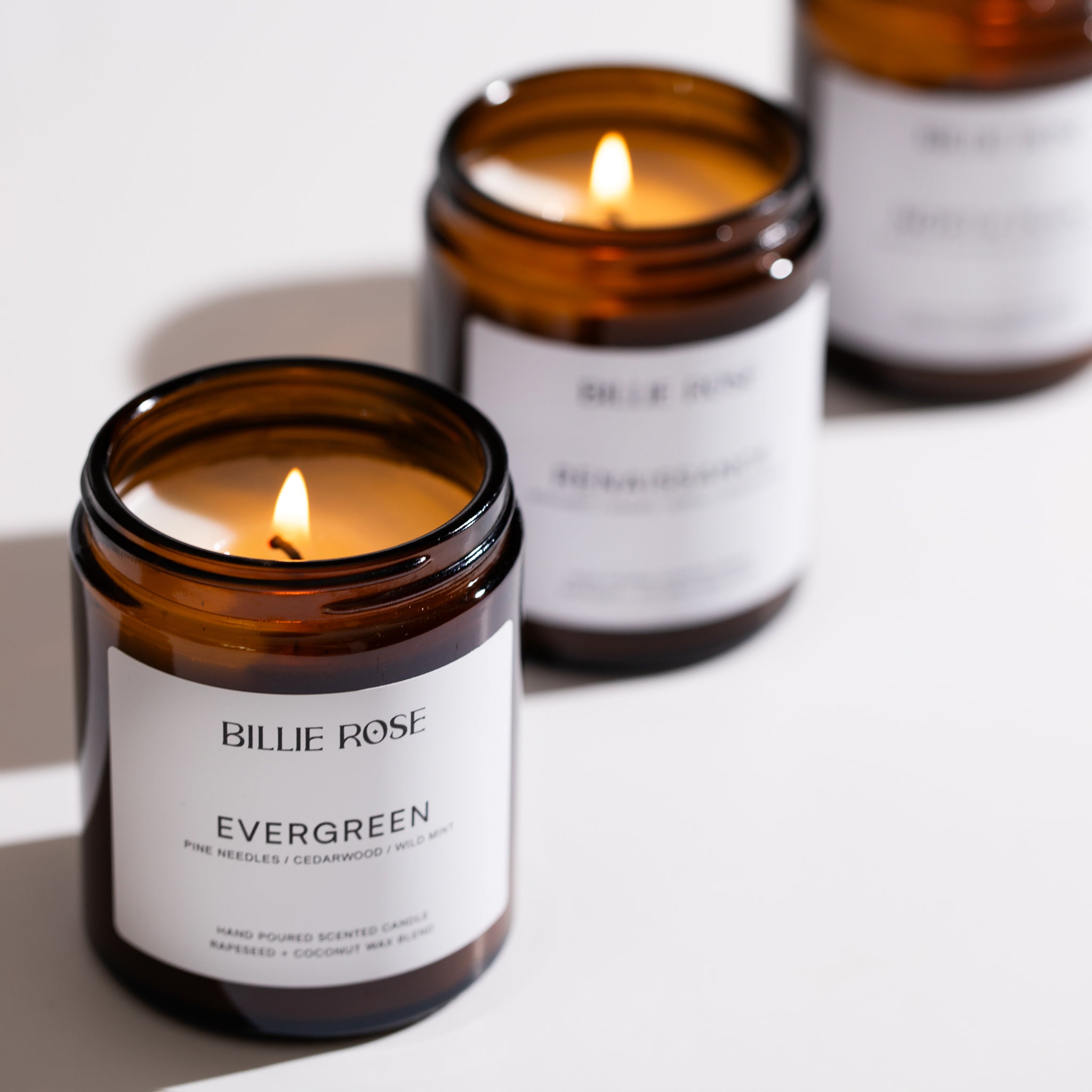 Three lit candles in amber jars with white labels on a light background