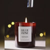 video of Billie Rose Nostalgia candle being put out with a candle snuffer and wisps of smoke rising against a dark brown background with blurred bokeh lights